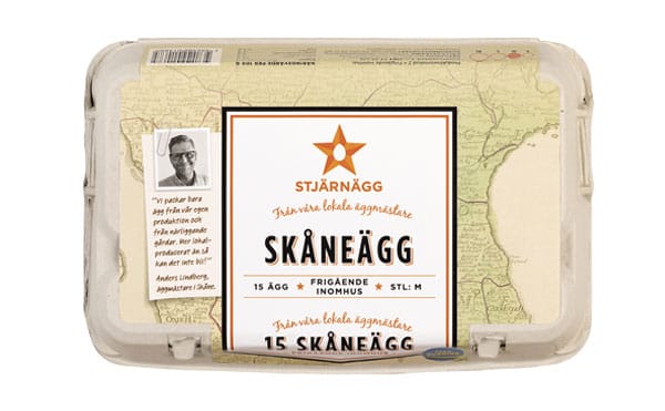 En kartong med Stjärnägg Skåneägg, innehållande 15 medelstora ägg från frigående höns. Förpackningen har en kartbakgrund, orange stjärnlogotyp och ett porträtt av en man med svensk text.