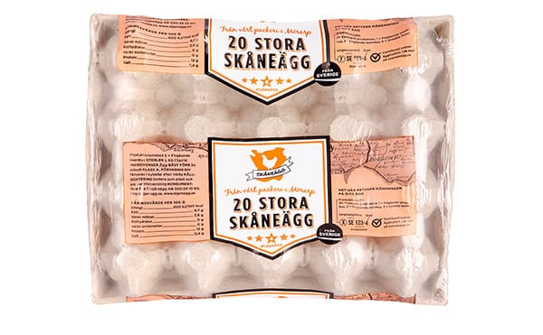 En kartong med 20 stora ägg, märkta 20 Stora Skåneägg med svensk text och en orange etikett med en illustration av en kyckling ovanpå den genomskinliga plastförpackningen som visar äggen inuti.