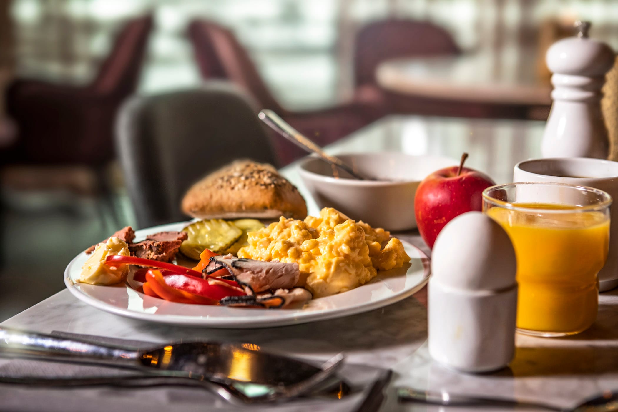 Stjärnägg En frukosttallrik med äggröra, skivade tomater, gurka, pålägg, bröd och ost, bredvid ett kokt ägg, äpple, glas med apelsinjuice, kaffekopp och pepparkvarn på ett bord.