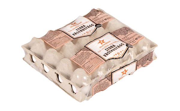 En kartong med ägg märkt "STORA VÄSTKUSTÄGG" är förpackad i en plastförpackning. Kartongen innehåller två lager ägg och har bruna och vita etiketter med text och stjärngrafik.