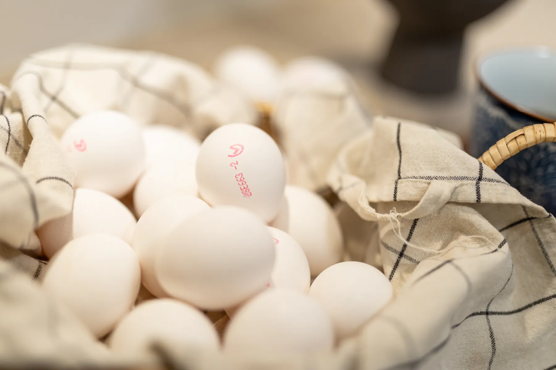Närbild på flera vita ägg med röda bläckstämplar som vilar i en korg klädd med ett vit- och svartrutigt tyg.
