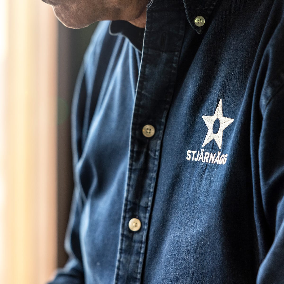En person som bär en mörkblå skjorta med knappar, broderad med en vit stjärna och texten STJÄRNÄGG.