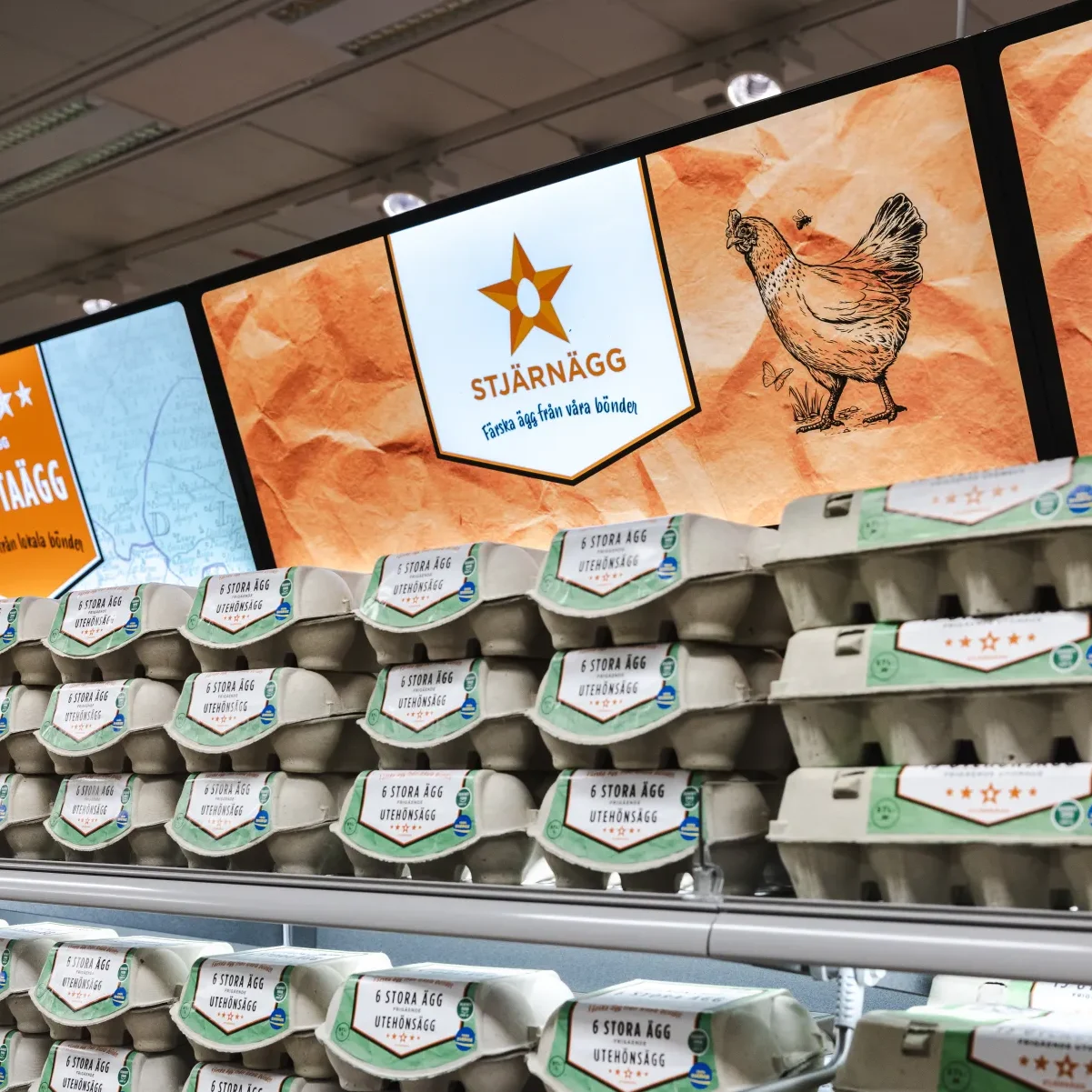 Stjärnägg i butik På butikshyllorna står äggkartonger staplade under digitala skyltar som visar en stjärna, en kycklingillustration och texten Stjärnägg på svenska, vilket indikerar ett äggmärke.