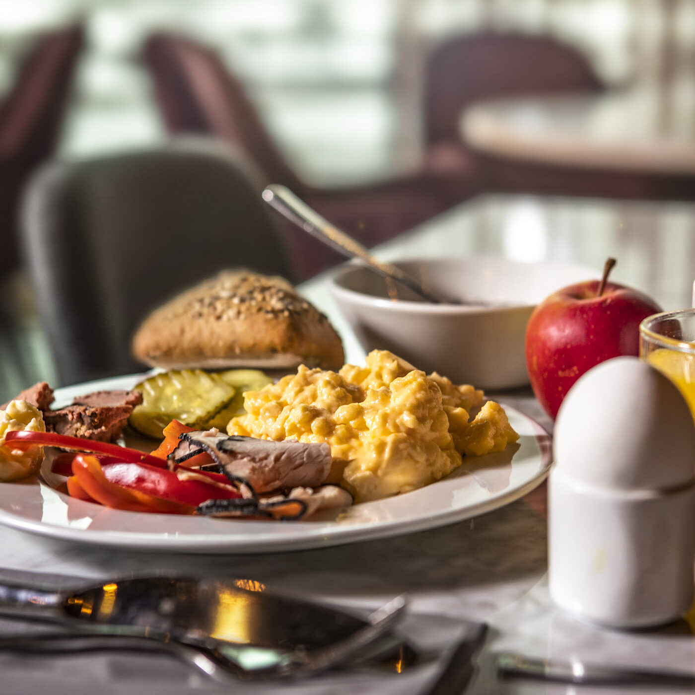 Stjärnägg En frukosttallrik med äggröra, skivade tomater, gurka, pålägg, bröd och ost, bredvid ett kokt ägg, äpple, glas med apelsinjuice, kaffekopp och pepparkvarn på ett bord.